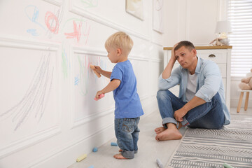 Upset father watching his little son drawing on wall at home - obrazy, fototapety, plakaty