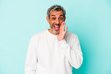 Middle age caucasian man isolated on blue background  shouts loud, keeps eyes opened and hands tense.