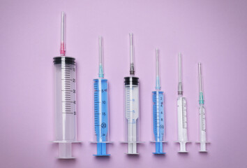 Disposable syringes with needles on violet background, flat lay