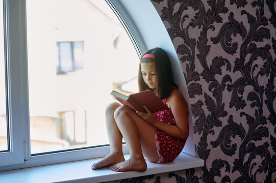 A girl is reading a book by the window