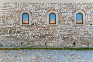 Three window with blue sky reflection on old castle block wall