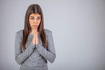 Obraz premium Young woman pleading and asking for something with clasped hands, positive emotional lady looking at camera with please expression, isolated over gray background