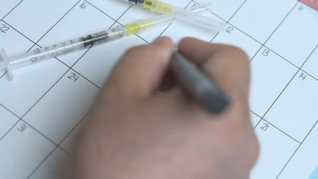 A person writing on calendar reminder - vaccine day. Writing on reminder date of immunization
