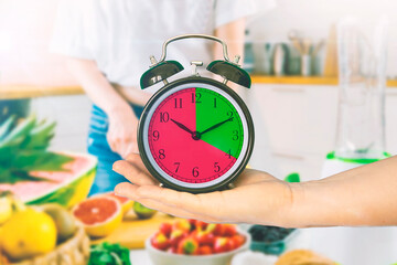 Hand holding a clock in a kitchen. Intermittent fasting concept.  Empty copy space for Editor's...