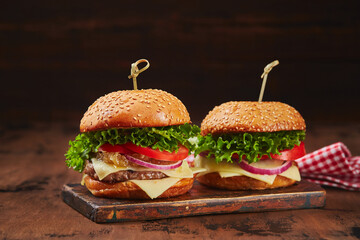 Two homemade burgers with beef, cheese and onion marmalade on a wooden board. Fast food concept, american food