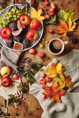 Dish with figs, apples and grapes and cup of coffee on wooden background with a warm sweater, scarf, autumn leaves and apples. Autumn background, top view.