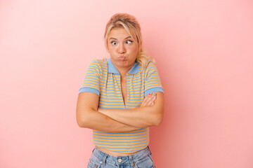 Young Russian woman isolated on pink background blows cheeks, has tired expression. Facial...