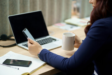 Caucasian business woman having a break with hot tea in the office. Hand holding white cup of coffee and checking e-mail or message today in the office