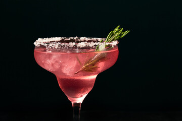 Alcoholic or non-alcoholic rosemary cocktail such as margarita, cosmopolitan or similar on a dark marble table