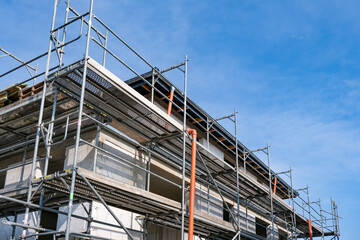 Konzept Hausbau: Seitliche Detailansicht eines eingerüsteten Rohbaus, Einfamilienhaus, mit extra viel blauem Himmel für Textfreiraum auf der rechten Seite