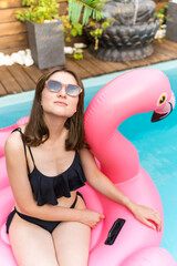 Model in glasses on a pink mattress in the pool. A young woman poses in the tropics. Summer party, joy