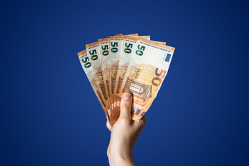 Hand holding three hundred euros in 50 euro bills with blue background - obrazy, fototapety, plakaty