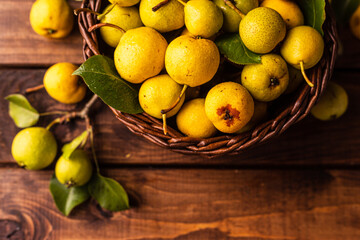 there are a lot of pears on the wooden table. In the middle is a cutting board on which pears are cut into two halves and a knife