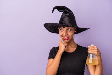 Young mixed race woman disguised as a witch holding potion isolated on purple background  relaxed thinking about something looking at a copy space.