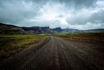 Driving on an unpaved road in summer in Iceland, moutains landscape, moody sky with dark clouds
