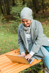 Young asian muslim woman using laptop at autumn park. Online education, online shopping and social networks concept.