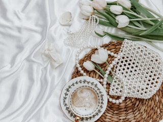 White tulips, coffee cup and woman accessory on silk background,  Morning coffee cup spring mood. Luxury romantic background. Woman morning, aesthetic concept. Top view, flat lay