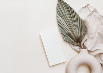 Wedding  mock-up. Blank greeting card and green palm leaves. Ceramic vase on beige neutral...