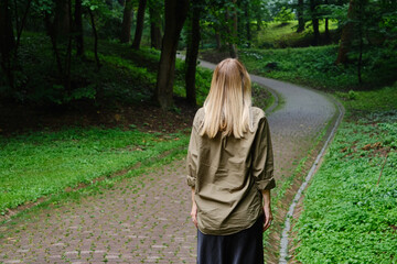 Beautiful woman walks along a path in a scenic park. Outdoor activities. Happy vacation outside the city. Summer walk in nature. Enjoy the weather and fresh air. Weekend in nature