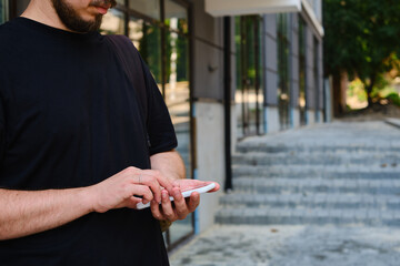 A man with a smartphone in his hands stands near the business center. A businessman is sending a text message or using an application on his mobile phone. Smartphone close up