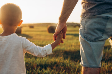 Father's and son holding hands at sunset field. Dad leading son over summer nature outdoor. Family,...