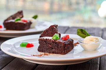 Slice of chocolate cake with candied fruit, mint and ice cream on a white plate and wooden background