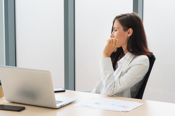Adult smart business woman sitting on the working desk and thinking about work in modern office room