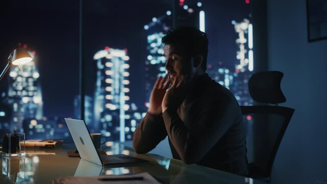 Portrait of Stressed Businessman Working on Laptop Computer in His Big City Office at Night. Overworked Tired Entrepreneur trying to Find Solution for Business Problems. Medium Arc Shot