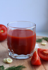 Fresh tomato juice in a glass with tomatoes, salt, garlic and herbs on a wooden board
