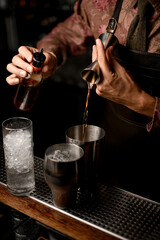 Fototapeta na wymiar hand of bartender holds bottle with dispenser and other hand pours drink from jigger into shaker glass