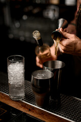 Fototapeta na wymiar hand of bartender masterfully pours drink from jigger into steel shaker glass