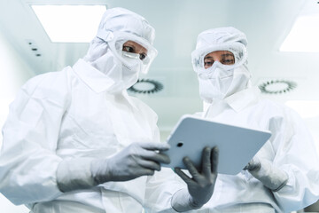 Low-angle shot of two Caucasian female researchers in full protective suits, with glasses, face...