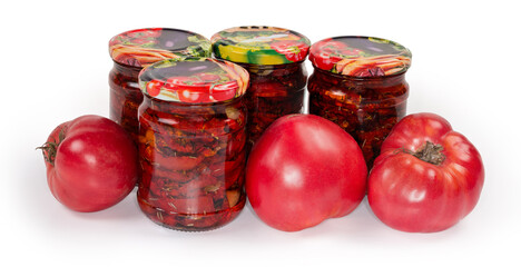 Dried tomatoes in oil in closed jars among fresh tomatoes