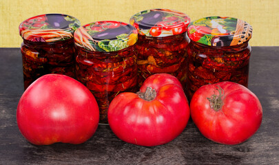 Fresh tomatoes and jars of dried tomatoes on dark surface