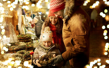 family, winter holidays and celebration concept - happy mother, father and little daughter buing wreath at christmas market on town hall square in tallinn, estonia