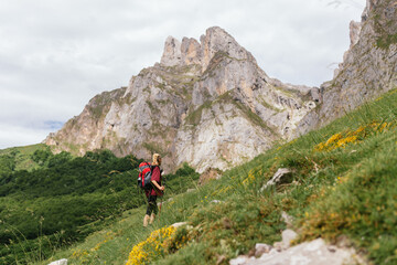 Fototapeta na wymiar Young traveler woman, with a backpack on her back, ascending a mountain during an excursion through the Picos de Europa National Park.