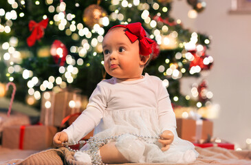 holidays and childhood concept - sweet baby girl with gifts at home over christmas tree lights