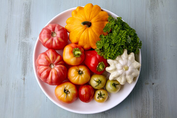 Ripe vegetables from the garden are laid out on a white plate