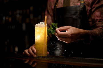 beautiful view of glass full of ice and cocktail with drinking straws and male hand with wet mint leaves