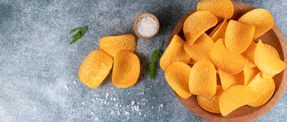 Top view of delicious homemade potato chips on a brown plate on gray background