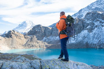 Man traveler with a heavy backpack on a cliff mountain above lake. Travel lifestyle, adventure