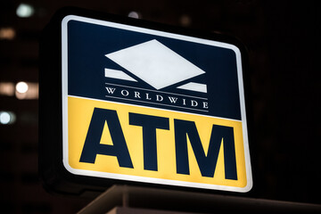 Glowing sign of ATM in city at night