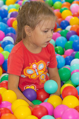 Fototapeta na wymiar Caucasian little girl of five years old looking aside among multicolor balls in play center