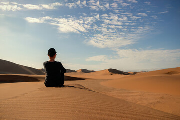A woman is sitting on the golden sand dune of the Namib desert.