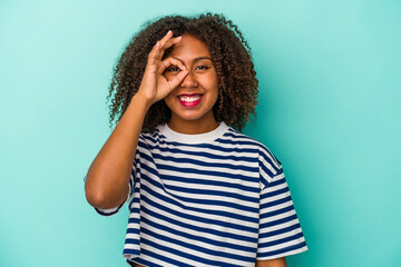 Young african american woman with curly hair isolated on blue background excited keeping ok gesture on eye.