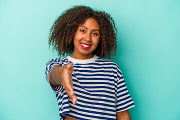 Young african american woman with curly hair isolated on blue background stretching hand at camera...