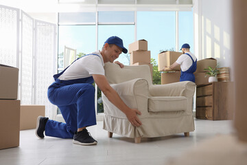 Fototapeta premium Moving service employees with armchair and cardboard boxes in room