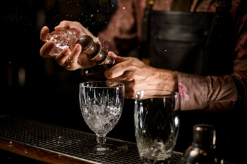 hand of male bartender holds ice cube and breaks it and the pieces fly in different directions