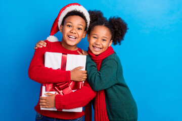Photo of funny sweet dark skin kids dressed sweaters headwear scarf holding gift smiling hugging...
