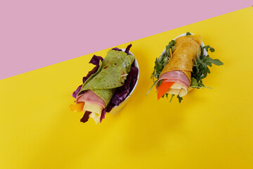 Flour tortilla wraps with ham, cheese and arugula on a yellow background.